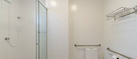 A bathroom with a glass shower enclosure, a toilet, a hand dryer, and a towel rack.