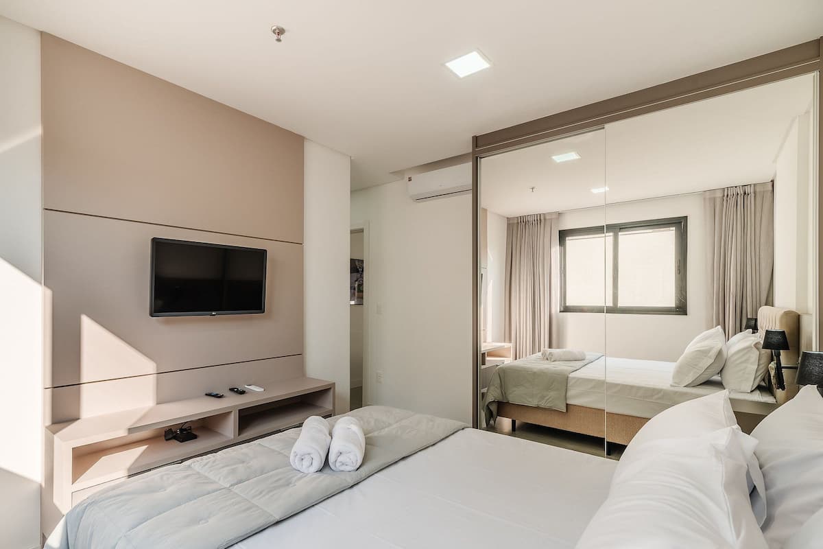 Une chambre d’hôtel avec un lit, un téléviseur fixé au mur, une table de chevet et un grand miroir qui reflète la pièce.