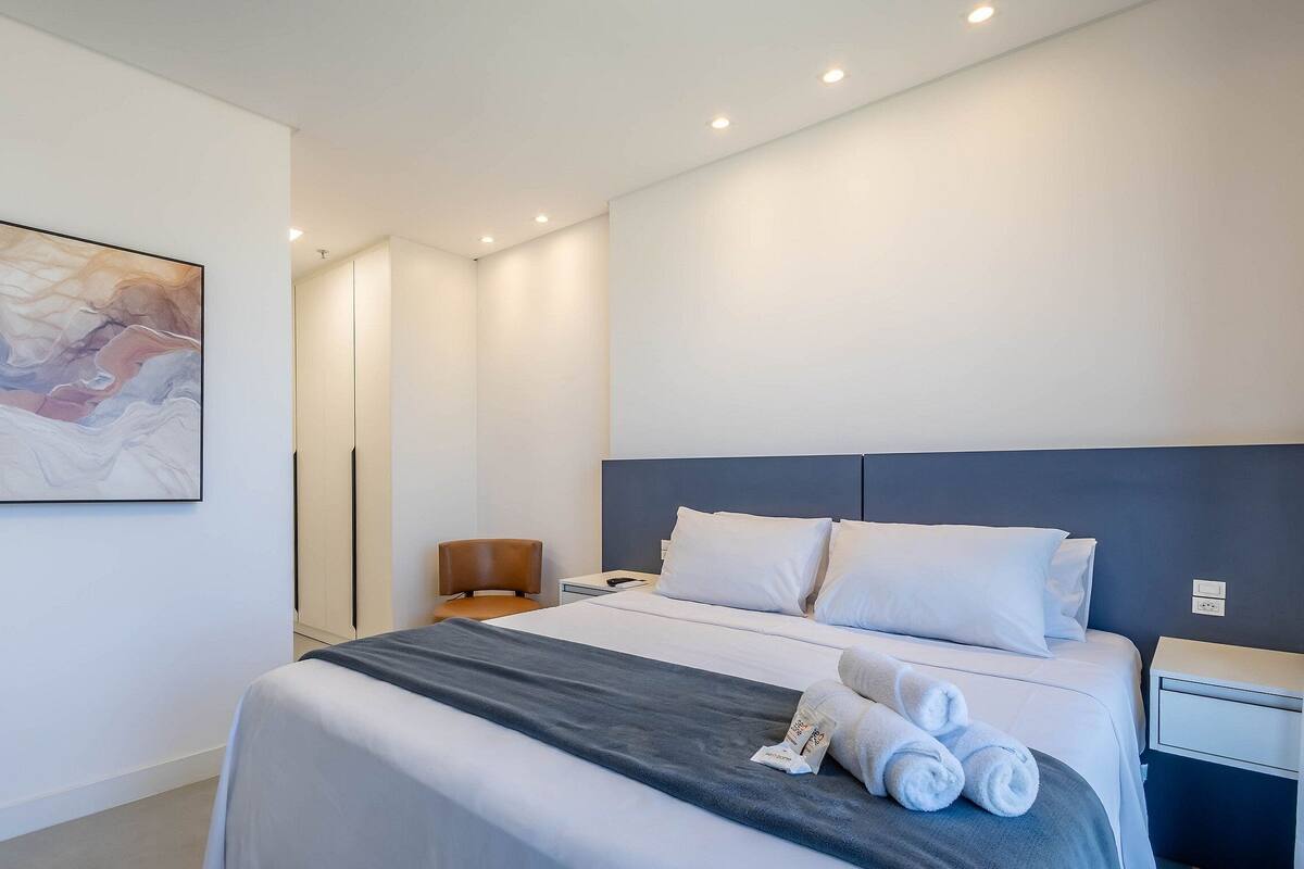 Une chambre d’hôtel moderne avec un grand lit, une table de chevet, une chaise et un tableau au mur.