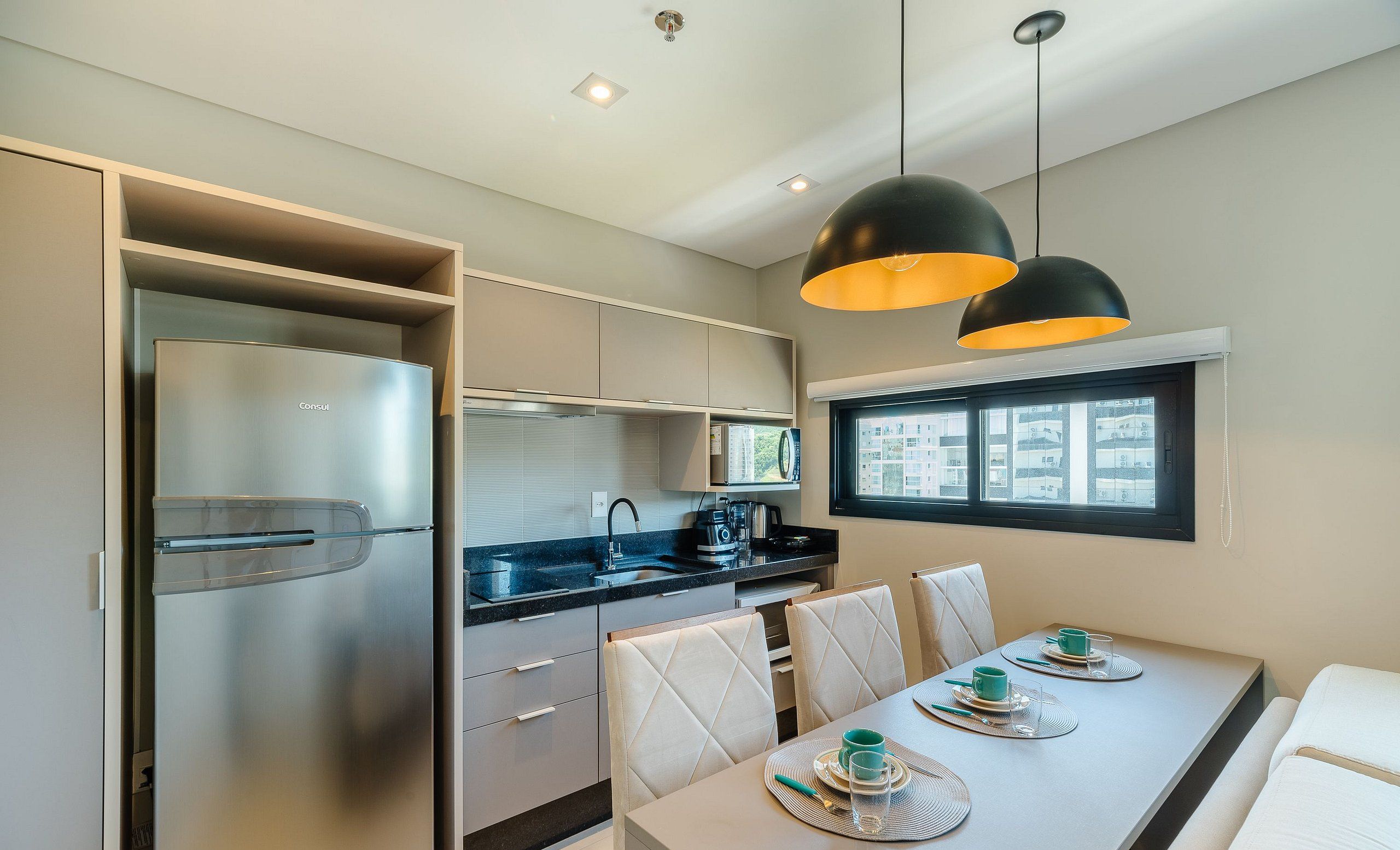 A modern kitchen with a built-in refrigerator, a dining area with a table set for four, and pendant lighting.