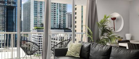 A modern living room with a black leather sofa, a round mirror, and a potted plant.