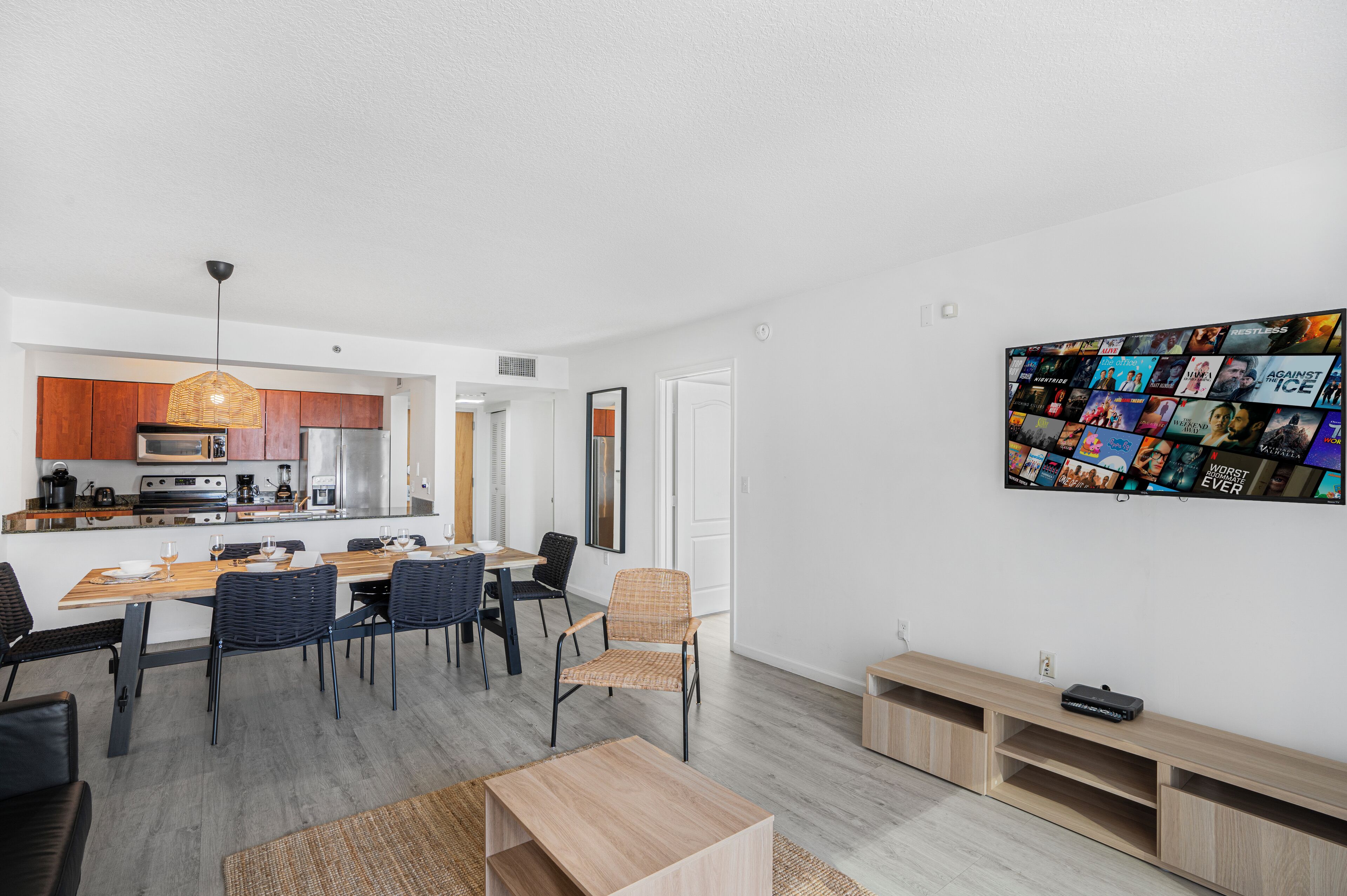 A modern living space with a kitchen, dining area, and a wall-mounted TV displaying movie posters.