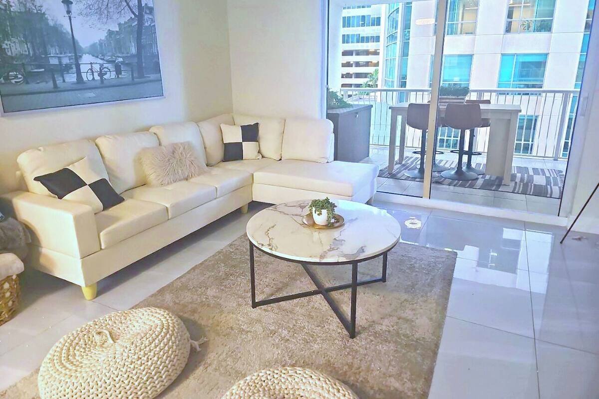 A modern living room with a white sectional sofa, a round coffee table, and a large window offering a view of a building.