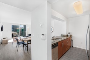 A modern kitchen with a dishwasher, sink, and wooden cabinets. There is a dining area with a table and chairs, and a view of the city through large windows. - 1200 Brickell - Miami stay - We Host (Miami)