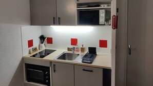 A compact kitchen with a microwave, stove, sink, and cabinets. - Cozy studio in Barcelonnette (Barcelonnette)