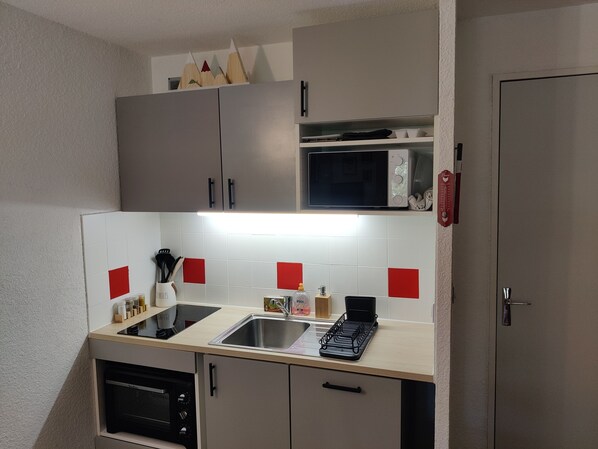 A compact kitchen with a microwave, stove, sink, and cabinets.