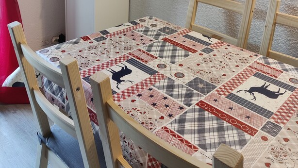 A dining area with a quilted tablecloth, wooden chairs, a television on a stand, and framed pictures on the wall. - Cozy studio in Barcelonnette (Barcelonnette)