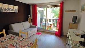 A cozy living room with a sofa, a dining table with a quilt, a small round table, and a TV stand. - Cozy studio in Barcelonnette (Barcelonnette)