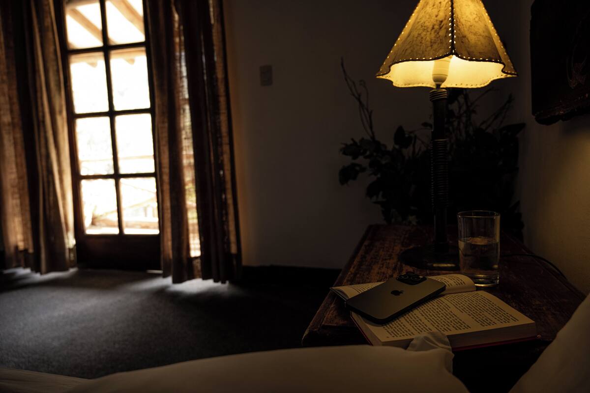 A dimly lit room with a lamp, a glass of water, and an open book on a wooden table.