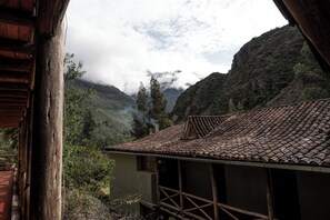 A rustic building with a tiled roof and wooden beams, surrounded by lush greenery and mountains in the background. - QASA Valle Sagrado by Nomad (Calca)