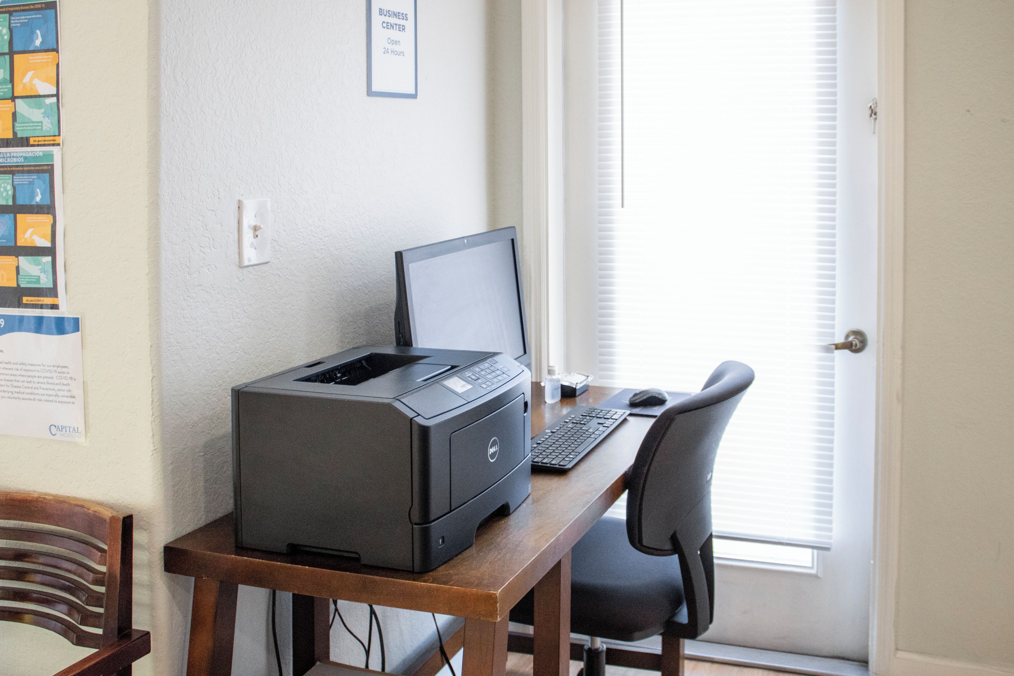 A home office setup with a desktop computer, printer, and keyboard on a wooden desk.