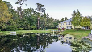 A pond with a wooden bridge, surrounded by lush greenery and a large yellow building with a flag. - Barefoot'n Resort Kissimmee Orlando (Kissimmee)