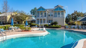 A swimming pool with lounge chairs and umbrellas, surrounded by a building with multiple balconies. - Barefoot'n Resort Kissimmee Orlando (Kissimmee)