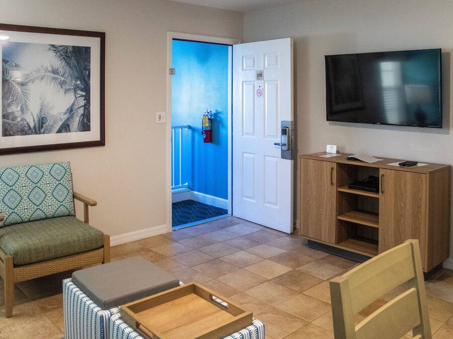 A room with a framed picture, a television, a wooden cabinet, a chair, and a door leading to a blue hallway.
