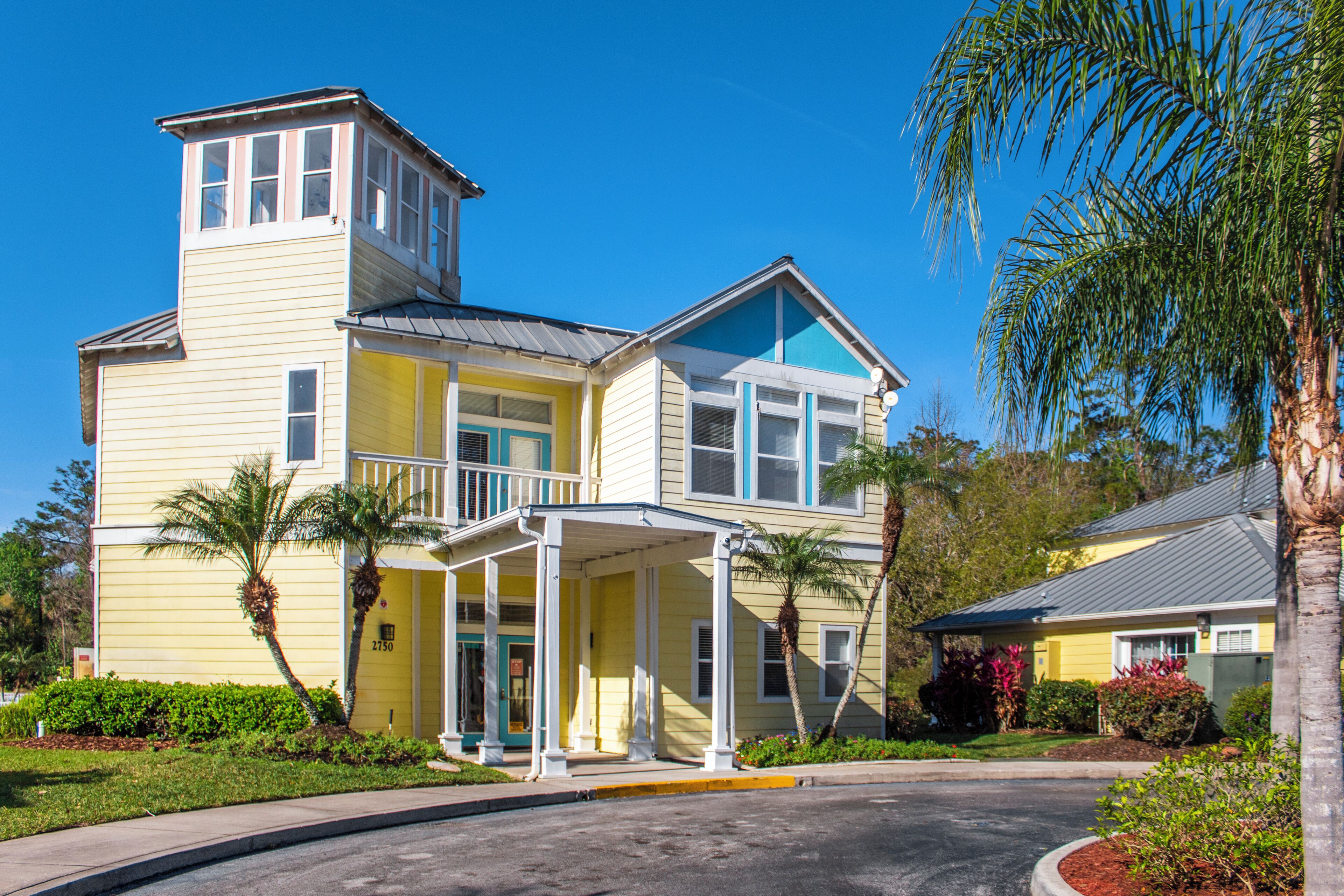 A two-story yellow building with a balcony, a covered porch, and a small tower-like structure on the roof.