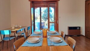 Zona pranzo con tavolo di legno apparecchiata per quattro persone, sedie blu e un'ampia finestra vista sul verde.