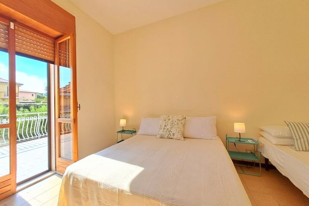 A bedroom with a large bed, two bedside tables with lamps, a sliding glass door leading to a balcony, and a small table with a chair.