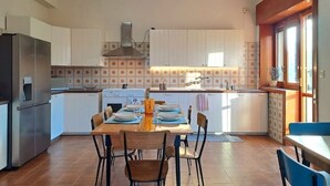 Cucina con mobili bianchi, isola centrale e zona pranzo con sedie.