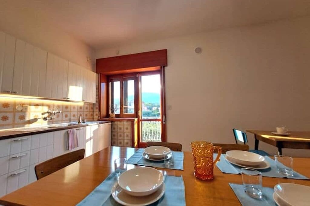 A kitchen with a dining table set for four, a window with a view, and white cabinets.