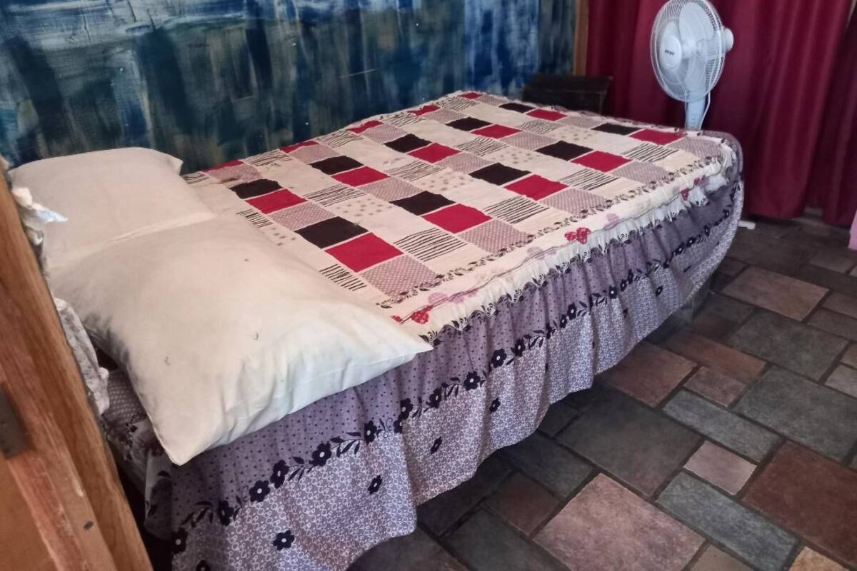 Ein Bett mit Decke, einem Ventilator und einem roten Vorhang.