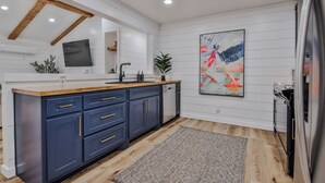 Een moderne keuken met een houten plafond, witte wanden, een groot kookeiland met blauwe kastjes, een spoelbak en een koelkast.