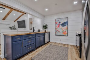 A modern kitchen with a wooden ceiling, white walls, a large island with blue cabinets, a sink, and a refrigerator.