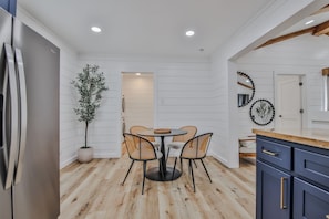 A modern kitchen with a round dining table, four chairs, a potted plant, and wooden flooring.