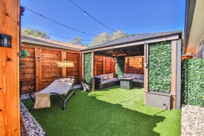 A wooden deck with a table and chairs, a bench, and a covered seating area with a green wall.