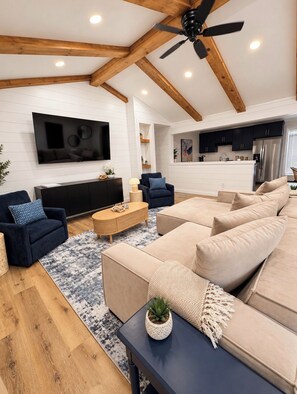 A modern living room with a large TV, sofas, a coffee table, and a ceiling fan.