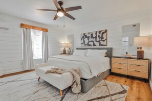 A bedroom with a bed, bedside tables, a ceiling fan, a large mirror, and a window with curtains.