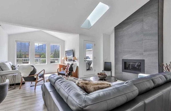 A modern living room with a fireplace, leather sofa, and a large window.