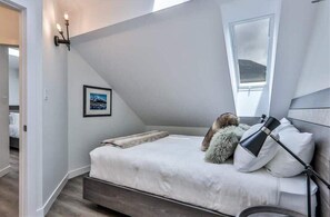 A bedroom with a bed, a nightstand, a lamp, a framed picture, and a window.