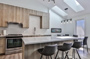 A modern kitchen with a large island, bar stools, and a skylight.