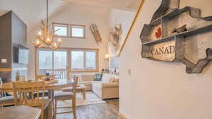A cozy interior with a dining area, a sofa, and a wall-mounted 'CANAD' sign. - Cascade Loft Mountain Views Hot Tub Pool (Canmore)