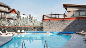 A swimming pool with lounge chairs, a stone wall, and a view of mountains. - Cascade Loft Mountain Views Hot Tub Pool (Canmore)