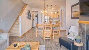 A modern kitchen with wooden cabinets, a stainless steel refrigerator, and a dining area with a wooden table and chairs. - Cascade Loft Mountain Views Hot Tub Pool (Canmore)
