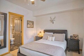 A bedroom with a large bed, a nightstand, a bedside table, a wall-mounted light, and a door leading to another room. - Cascade Loft Mountain Views Hot Tub Pool (Canmore)