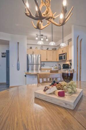 A modern kitchen with wooden cabinets, a stainless steel refrigerator, and a dining area with a wooden table set for a meal. - Cascade Loft Mountain Views Hot Tub Pool (Canmore)