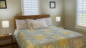 Une chambre à coucher avec une tête de lit en bois, une couvre-lit matelassée, deux lampes de chevet et une fenêtre avec des stores.