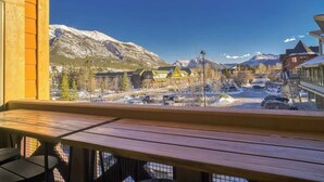 A wooden deck with a view of a snowy mountain town, featuring buildings and parked cars.