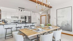 A modern kitchen with white cabinetry, a wooden dining table, and a chandelier.