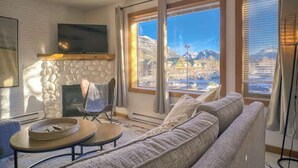 A living room with a stone fireplace, a large window with a mountain view, a sofa, and a television.