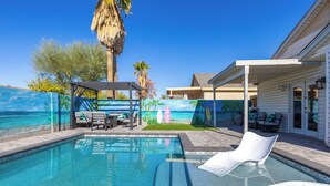 A swimming pool with lounge chairs, a pergola, and a mural of a beach scene. - Seaside Cottage in walking distance of downtown Gilbert with charming pool. (Gilbert)