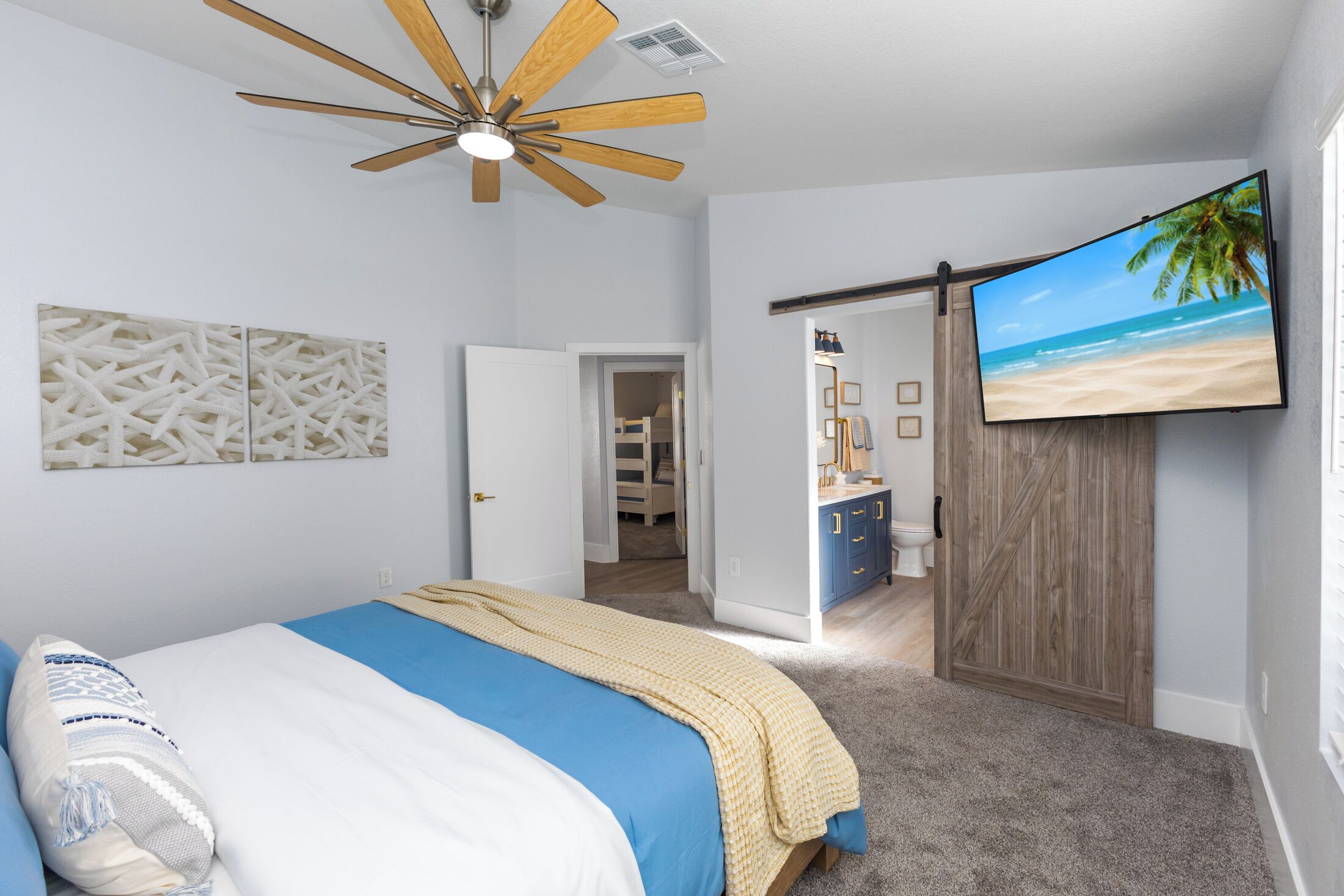 A bedroom with a bed, a ceiling fan, a TV displaying a beach scene, and a wardrobe.