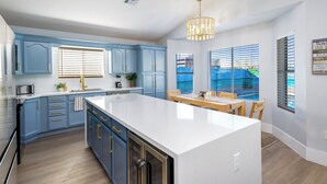 A modern kitchen with blue cabinets, a white island, and a dining area with a view of the outdoors. - Seaside Cottage in walking distance of downtown Gilbert with charming pool. (Gilbert)