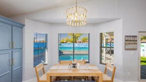 A dining area with a wooden table, chairs, a bench, a chandelier, and a view through large windows. - Seaside Cottage in walking distance of downtown Gilbert with charming pool. (Gilbert)