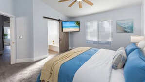 A bedroom with a bed, a ceiling fan, a TV, and a beach-themed painting. - Seaside Cottage in walking distance of downtown Gilbert with charming pool. (Gilbert)