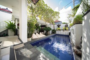 A swimming pool surrounded by a white building with a tiled deck, potted plants, and a statue. - Gilang Balangan (Jimbaran)