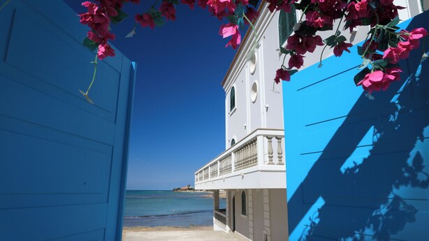 Een gebouw aan de kust met een balkon, uitzicht op zee, een heldere lucht en het strand.