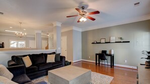 Ein geräumiges Wohnzimmer mit einem dunkelgrauen Sofa, einem beige-farbenen Couchtisch und einem Deckenventilator.